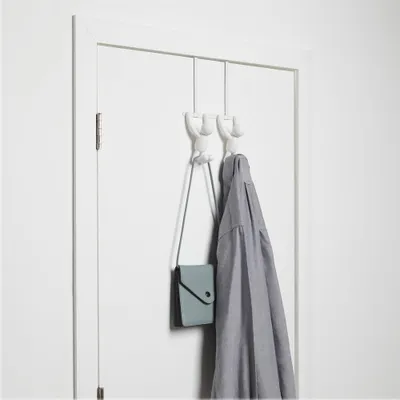 Two white cartoon-like hooks attached to a white door, with a gray shirt and a small teal purse hanging from them.