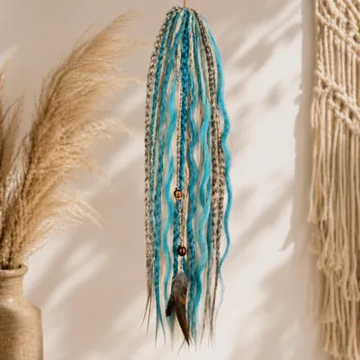 Türkis- und beigefarbene synthetische Dreadlock-Extensions mit Perlen und einer Feder, hängend an einer hellen Wand