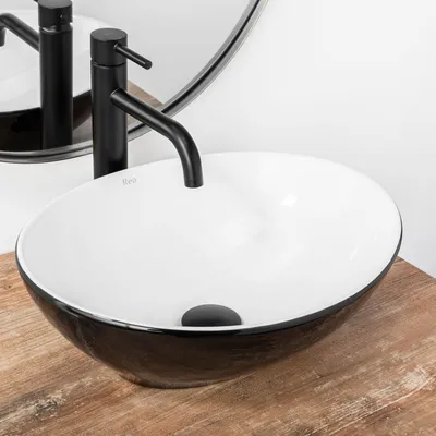 A close-up shot of a modern bathroom sink on a wooden countertop, with a black faucet and a circular mirror in the background.
