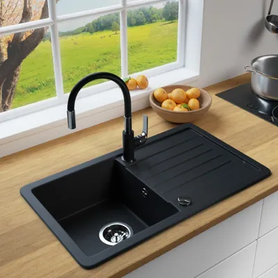 A black granite kitchen sink with a modern faucet is shown on a wooden countertop, with a bowl of fruit and a window overlooking a green landscape in the background.