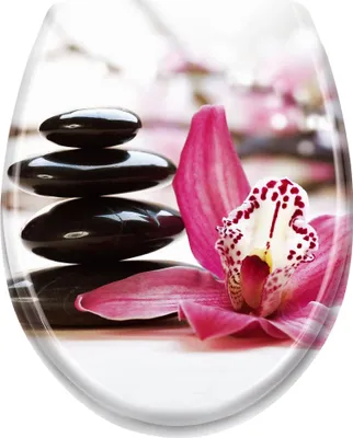 A stack of smooth black stones and a pink orchid are arranged on a white surface, with a blurred background of pink flowers.