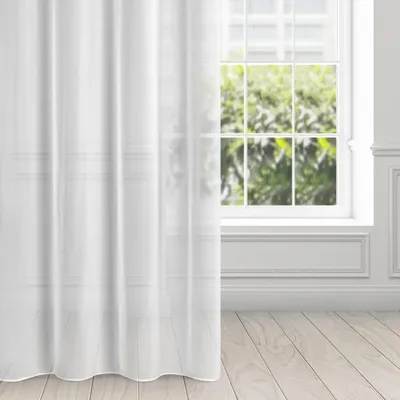 A white sheer curtain hangs in front of a window with a view of green trees.