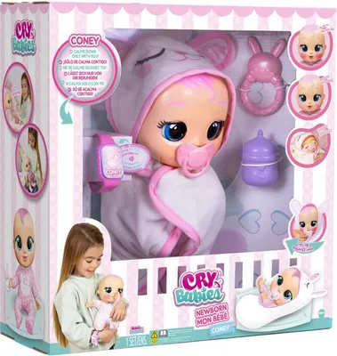 The image shows the packaging of a Cry Babies doll, with the doll and its accessories visible inside. A child is also shown holding a smaller version of the doll.