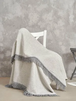 A blanket draped over a white chair against a textured gray wall.