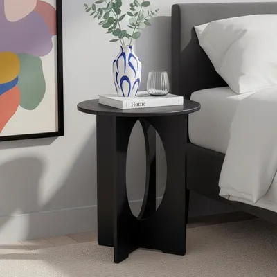 A black side table with a vase, book, and glass on it, next to a bed.