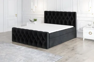 A black boxspring bed with a white mattress and a grey rug in a well-lit room.