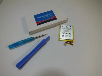A battery replacement kit for an iPod Nano 7G, including a battery, a screwdriver, and a plastic prying tool, laid out on a light gray surface next to its packaging.