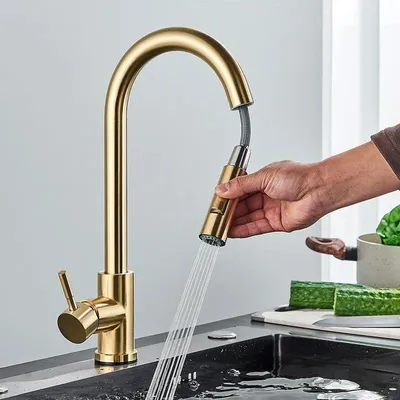 A person's hand is holding a gold kitchen faucet sprayer over a sink.