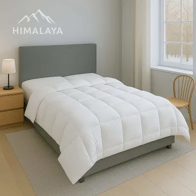 A white comforter is laid out on a bed with a grey headboard in a bedroom setting.