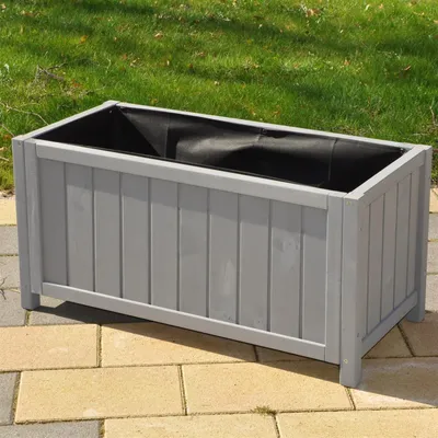 A gray rectangular planter box with a black liner sits on a patio with grass in the background.