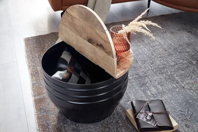 A round storage table with a wooden lid is placed on a rug next to a leather notebook.