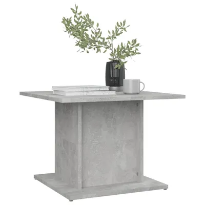 A square coffee table with a concrete gray finish, shown from a slightly elevated front-left angle. A black vase with green foliage and a gray mug are placed on top of the table.