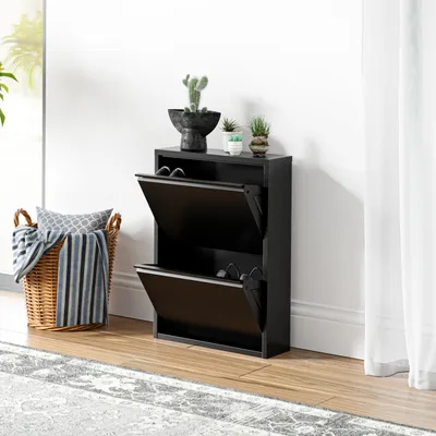 A black shoe cabinet with two open flip-down doors, placed on a wooden floor next to a woven basket with blankets and pillows.