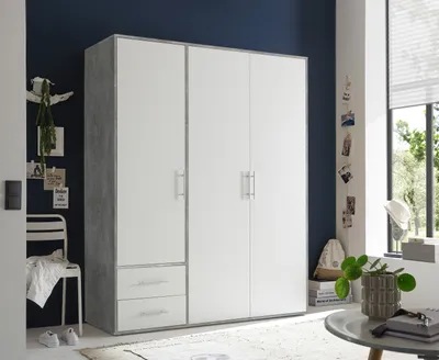 A white wardrobe with gray accents is placed against a dark blue wall. There are two drawers at the bottom and three doors on the main body. A white chair with a folded blanket is on the left. A window is on the right.