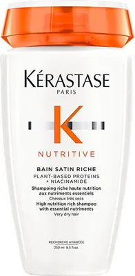 A white bottle of Kérastase shampoo with an orange cap.