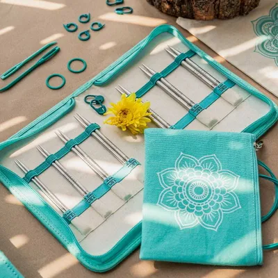A knitting set laid out on a textured surface with a yellow flower.