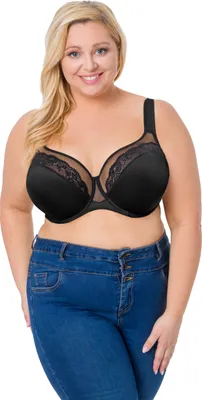 A woman wearing a black bra and blue jeans, posing against a white background.