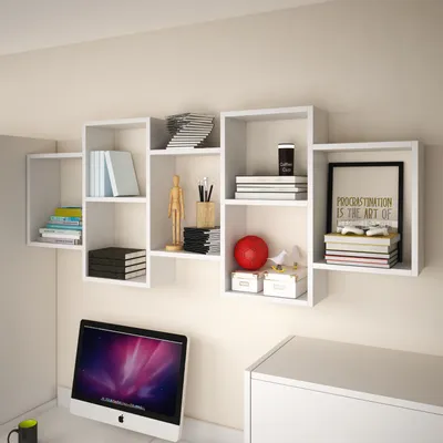 A white modular wall shelf unit filled with books, decorative items, and art supplies, mounted on a light beige wall above a computer.