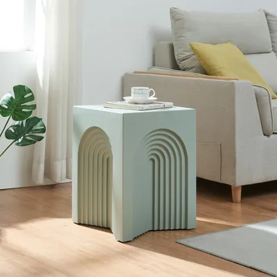 A light green side table with an arched design sits next to a beige sofa in a living room.