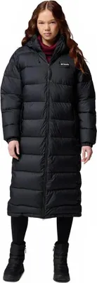 A woman wearing a long black puffer coat and black boots, standing against a white background.