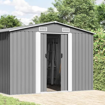 A grey metal shed with double doors, set in a garden with trees and a paved patio.