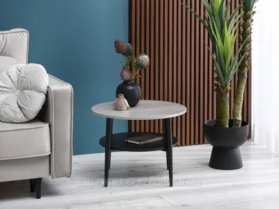 A round coffee table with a book and vase on it, next to a sofa and a large plant.