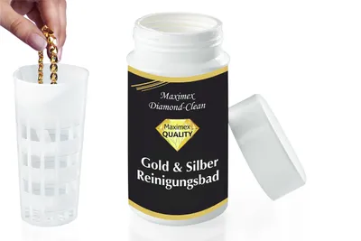 A hand is shown holding a gold chain over a white plastic container, next to a bottle of gold and silver cleaning solution.