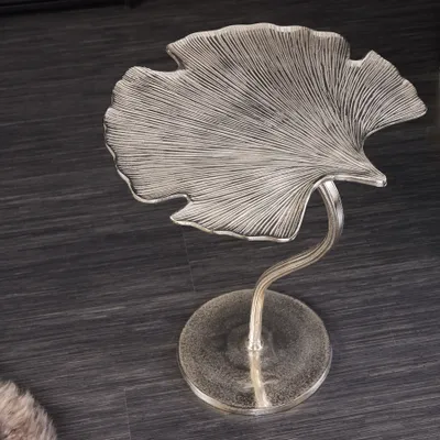 A decorative side table shaped like a ginkgo leaf, made of silver-colored metal, placed on a dark wooden floor.