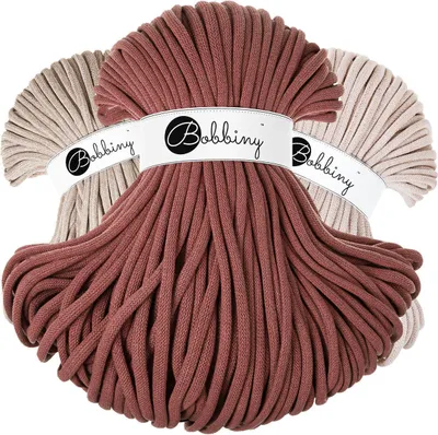 Three skeins of Bobbiny Jumbo cord in beige and rose colors, with branded labels.