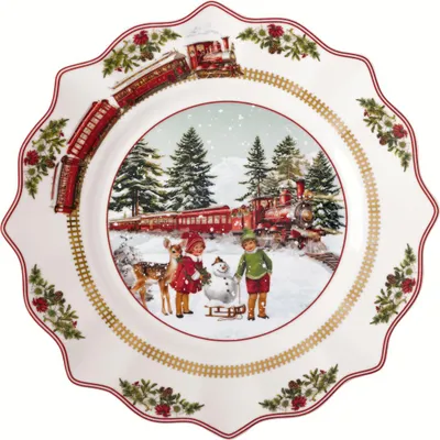 A Christmas-themed plate with a winter scene featuring a train, children, a snowman, and a deer.