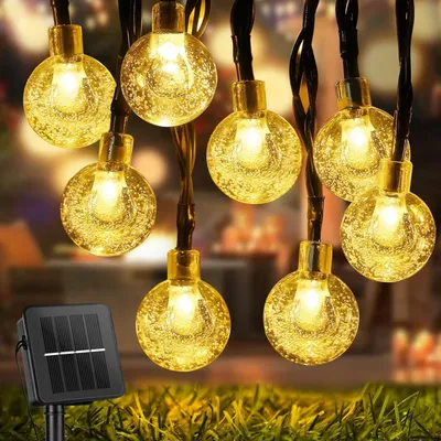 Solar-powered string lights with round bulbs are displayed outdoors on grass, with a solar panel in the foreground.