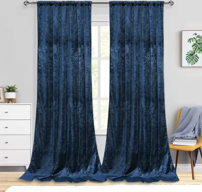 A room with blue velvet curtains hanging over a window, a white dresser, and a yellow chair with a blanket.