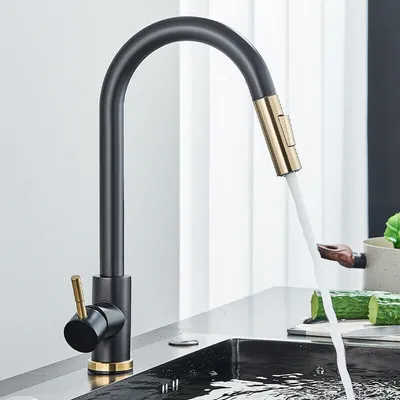 A modern kitchen faucet with a pull-down sprayer is shown in use, with water flowing into a sink. Cucumbers and other kitchen items are visible in the background.