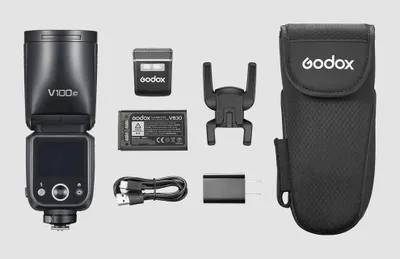 A flat lay of camera flash accessories, including the flash unit, battery, charger, and carrying case.