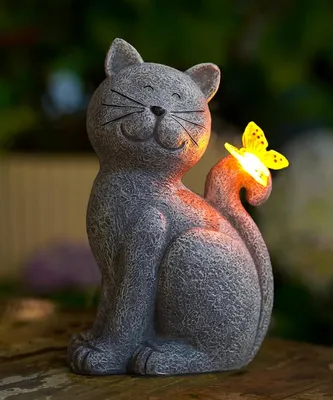 A solar-powered garden statue of a cat with a butterfly on its tail, lit up at night.