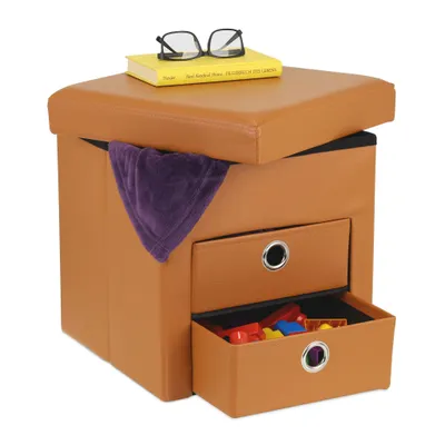A brown storage ottoman with two drawers, a yellow book, and glasses on top, and a purple blanket draped over the side. The bottom drawer contains colorful toy blocks.