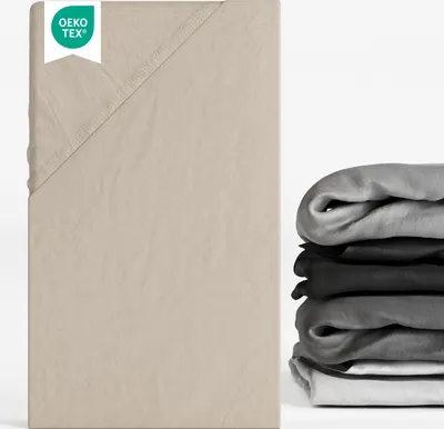 A close-up of a beige fitted sheet with a stack of folded sheets in various shades of gray and black on the right side.