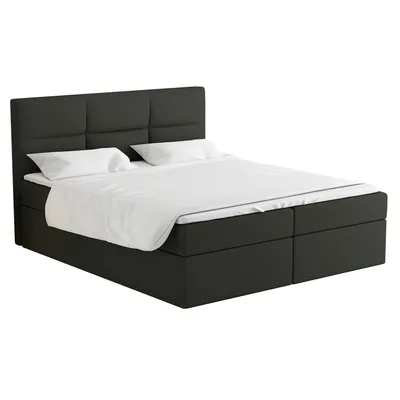 A studio shot of a gray box spring bed with white bedding and pillows.