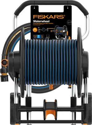 A Fiskars Waterwheel XL hose reel is shown against a white background. The product is a manual hose reel with a black frame and blue hose. It has a silver handle and orange accents. A product tag is attached to the handle.