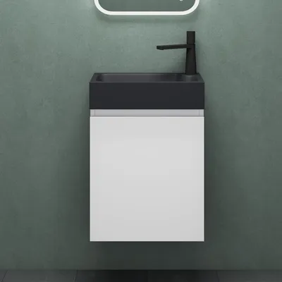 A modern bathroom vanity with a black sink and white cabinet against a textured green wall.