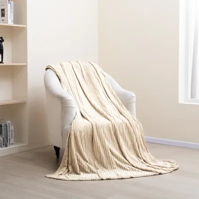 A plush blanket draped over an armchair in a room with a bookshelf and a window.