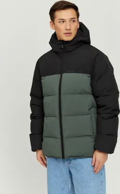 A man wearing a puffer jacket and jeans, posing against a plain background.
