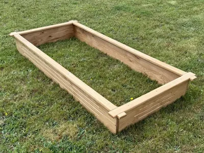 A wooden raised garden bed is placed on a grassy lawn.