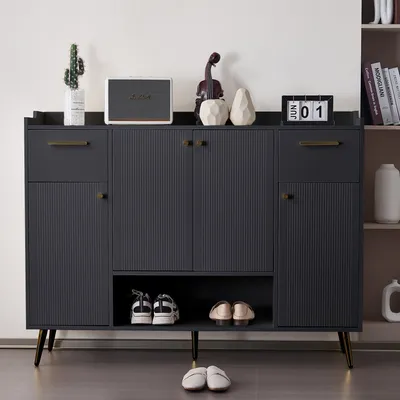 A dark gray shoe cabinet with gold accents, featuring drawers and doors, is shown in a room setting. Decorative items and shoes are placed on and inside the cabinet.
