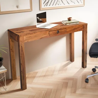 A wooden desk with a laptop and books on it, placed against a wall with artwork.