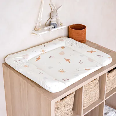 A baby changing mat with a pattern of suns, clouds, and birds, placed on top of a wooden storage unit with woven baskets.