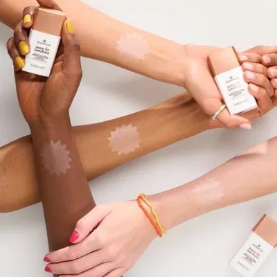 Multiple arms with different skin tones are shown, with swatches of a product applied to them. Two small bottles of the product are also visible.