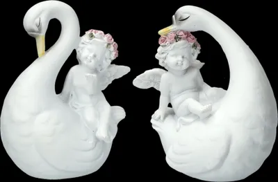 Two white ceramic figurines of cherubs sitting on the backs of white swans, with pink floral wreaths on their heads.