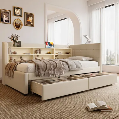A beige daybed with storage drawers and a bookshelf headboard is shown in a well-lit room with sheer curtains and decorative items on the shelves.