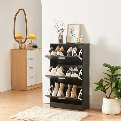 A shoe cabinet with multiple shelves and flip-down doors, filled with various shoes, is shown in a room with a mirror and a plant.